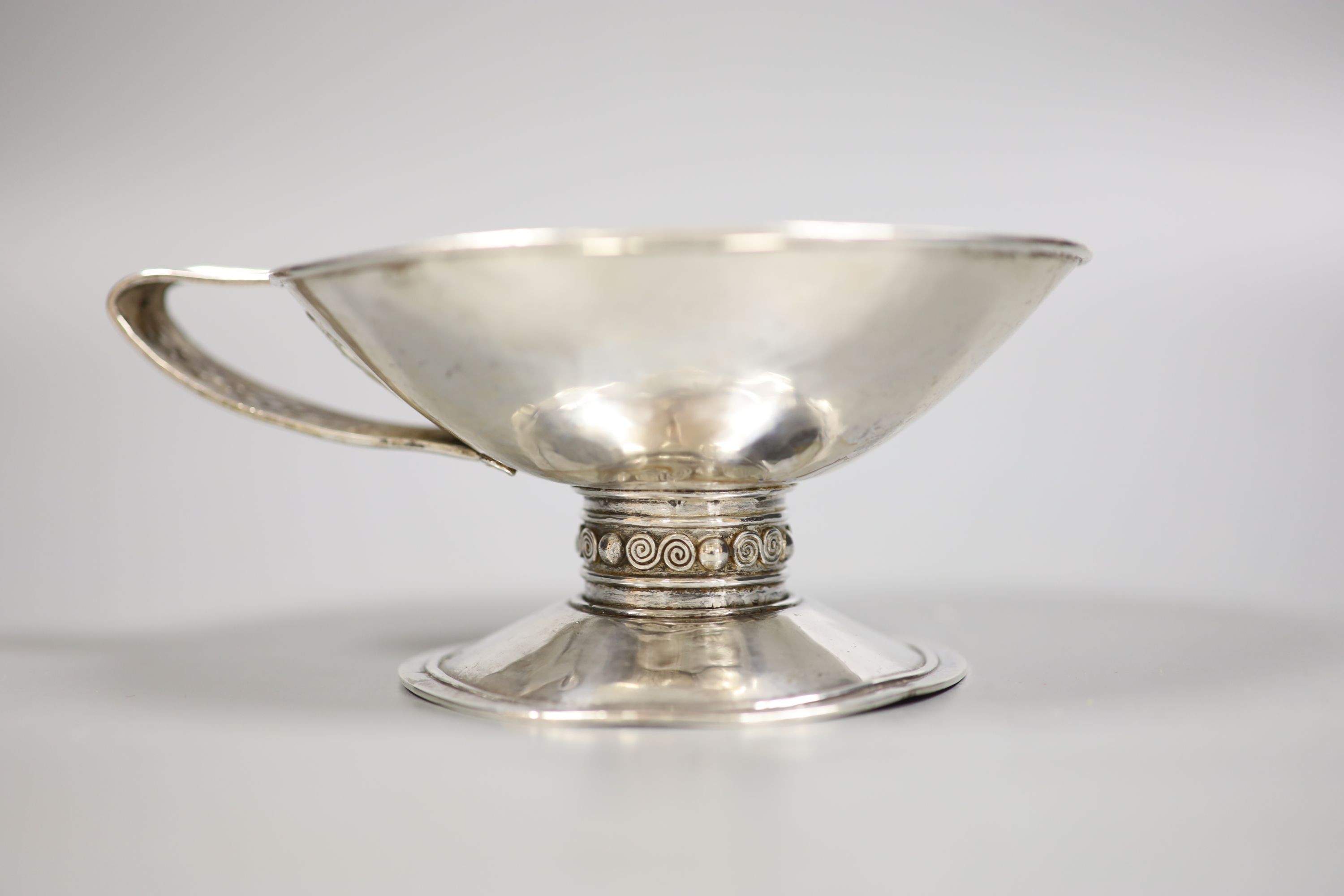 An Arts & Crafts planished white metal single handled pedestal cup, diameter 13.5cm, 6.5oz.